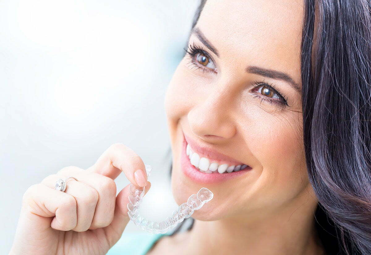 Invisalign orthodontics concept - Young attractive woman holding - using invisible braces or trainer.